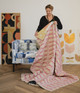 Véronique de Soultrait holding a sustainable quilt featuring her ‘Mikado’ embroidery in hot pink; her original artwork displayed in the background, with a chair upholstered in Galaxie fabric from the Atelier Véronique collection.